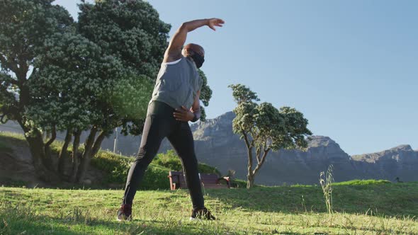 Senior african american man wearing face mask exercising stretching in countryside