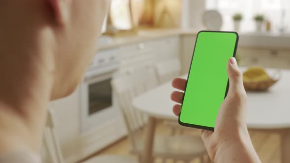 Back View of Man at Kitchen Room Sitting on a Chair Using Phone With Green Mockup Screen Chroma Key