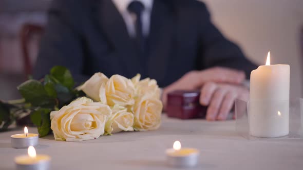 Bouquet of Yellow Roses Lying on the Table with Candles Standing Around. Unrecognizable Man in Suit