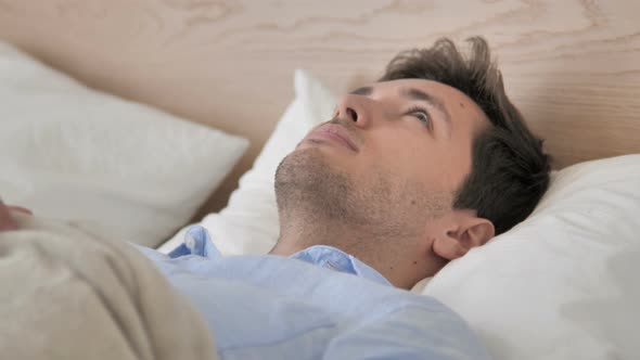 Pensive Young Man Thinking while Lying in Bed