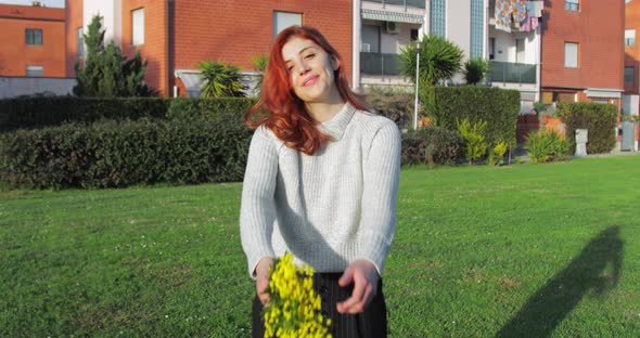 Young Girl Shows Yellow Mimosa Flowers in a Park Near the Houses