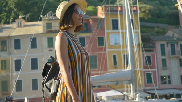 A woman walking wearing hat and backpack purse traveling, Portofino, Italy, luxury resort, Europe.