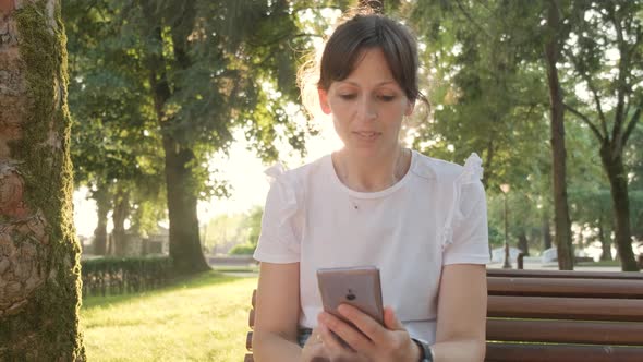 A Woman Using Her Phone While Sitting In the Park, Handheld Shot