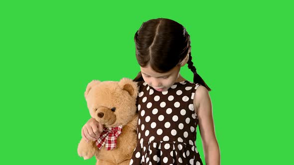 Shy Little Girl in Polka Dot Dress Hugging Her Teddy Bear While Walking and Looking Down at Her Feet