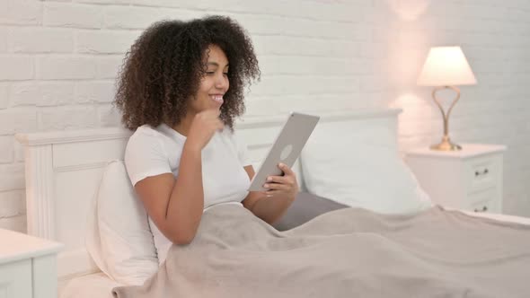 Excited Young African Woman Celebrating on Tablet in Bed