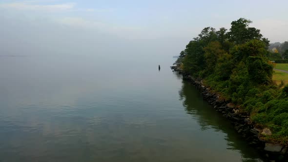 A low angle view of a calm river during a peaceful sunrise. It is misty and the drone is flying righ