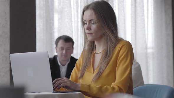 Brunette Beautiful Caucasian Woman Typing on Laptop Keyboard and Turning To People at the Background