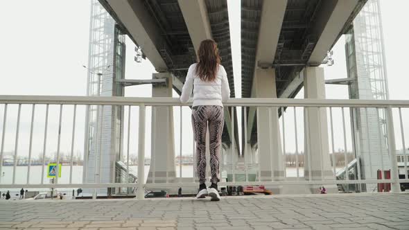 Young athletic girl in white jacket and leggings runs to the parapet and stopped.