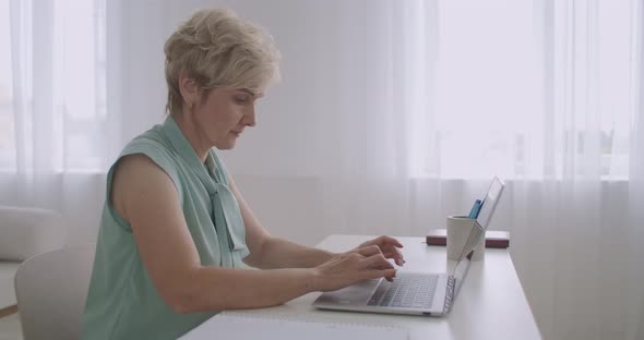 Aged Woman Is Chatting at Social Nets By Internet, Using Laptop, Typing Message on Keyboard, Sitting