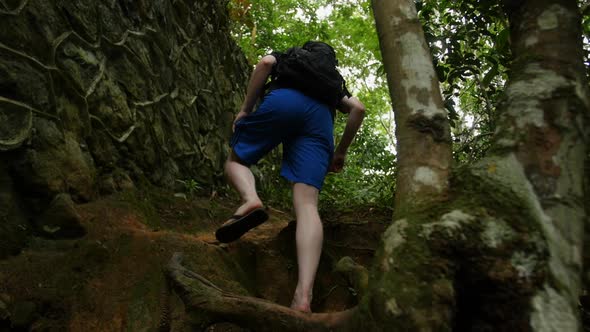 Caucasian maie hikes up a hill with roots near an old abandoned bridge in the rain forest on Ihla Gr