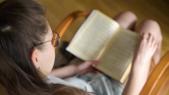 a girl with glasses is reading a book in daylight. Selective focusing on glasses.