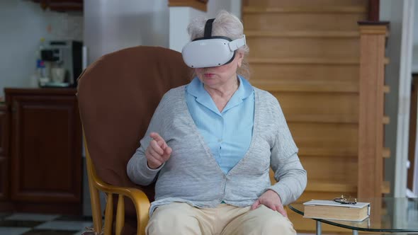 Absorbed Caucasian Senior Woman in VR Headset Gaming Online Sitting at Home in Living Room