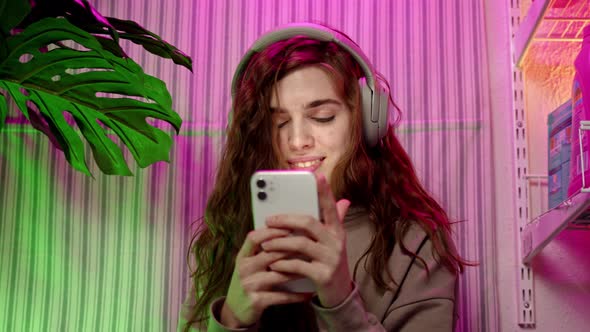 Close Up Young Woman with Brown Hair Listens to Music on Headphones and Text on Phone