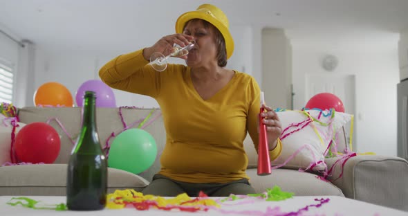 African american senior woman celebrating with champagne and party blower, on new year's video call