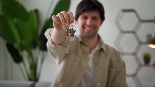 A Young Man Holding the Keys to a New House in His Hands Stands with a Happy Face and Smiles with a