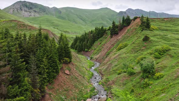 Flying Above Small Ravine With River In The Mountains