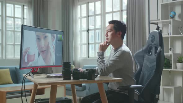 Asian Cameraman Thinking While Using Desktop Computer For Editing Photo At Home