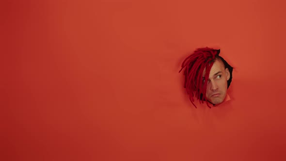 Young Man with Red Hairstyle Sticking Out of Hole of Orange Background