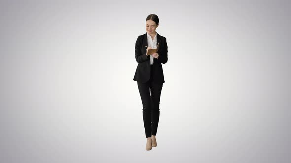 Concentrated Woman in a Suit Writing Business Ideas in Her Notepad While Walking on Gradient