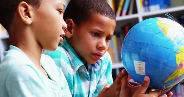 Schoolkids looking at globe in library at school