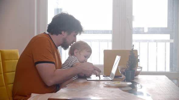 Alone Father Tries to Work Using a Laptop with His Baby Sitting on His Knees