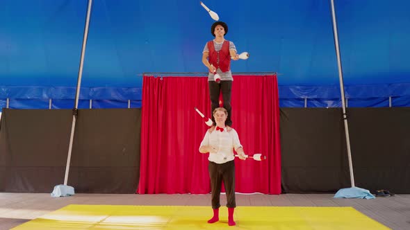 Male circus artists juggling with clubs standing on each other