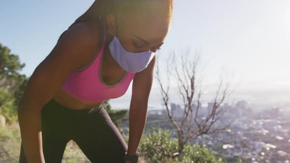 Tired african american woman wearing face mask taking a break from running outdoors