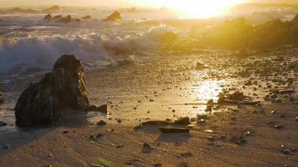 Small waves crashing onto beach during golden sunset in background.