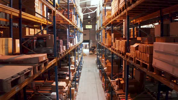 Man leaving a long warehouse aisle with stacked packed boxes,aerial.