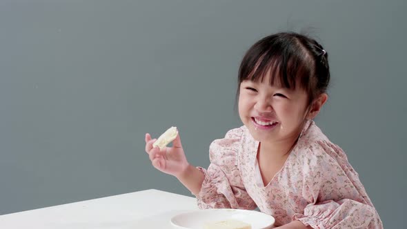 Happy little Asian girl rubs her eyes, smile, and enjoy eating crispy butter toast at home.
