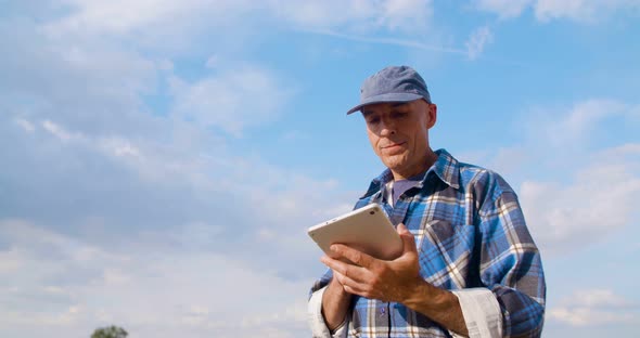 Farmer Using Digital Tablet at Farm Against Blue Sky and Clouds.