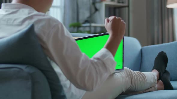 Man Celebrating While Lying On Sofa And Using Green Screen Laptop In The Living Room