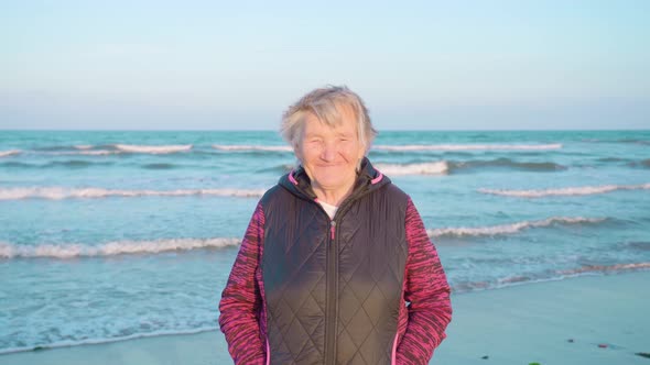 Old Woman Smiles Happily Under Wind Standing on Sea Beach