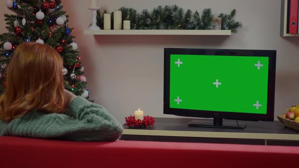 A red-haired girl watching Green Screen Mockup TV in a Chrismas decorated living room.
