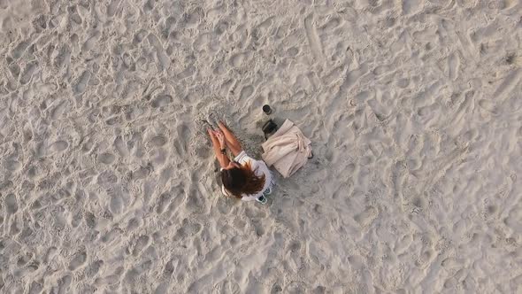 Footage From Above Romantic Tanned Girl with Long Dark Hair Sitting on Seashore Burying Feet Into