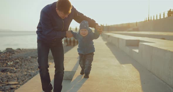 Happy Dad Walks with the Little Son Along the Coast