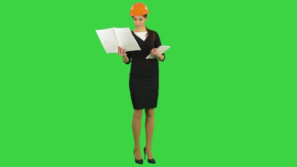 Female Construction Engineer in Helmet Holding Blueprints and Using Tablet on a Green Screen, Chroma