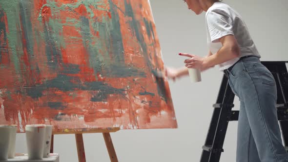 Female Artist Draws with a Brush on a Large Canvas in a White Room a Talented Artist Draws a Color