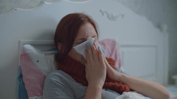 Sick Young Woman Laying in Bed. Woman with Warm Scarf on Neck Coughs and Blows Her Nose. Hand with