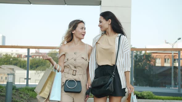 Dolly Shot of Happy Girls Shopaholics Walking in the Street Carrying Shopping Paper Bags and Talking