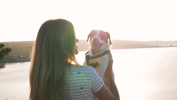 Young Attractive Woman Playing with a Dog Jack Russell in the Meadow at Sunset with Sea Background