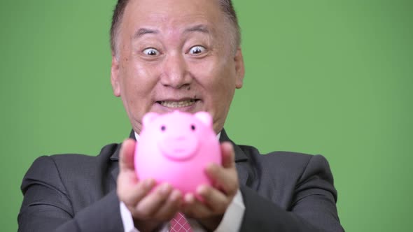 Mature Japanese Businessman Holding Piggy Bank