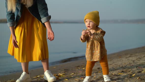 Mom Holds Her Daughter By the Hand and Teaches Her To Walk on Beach