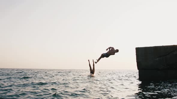 Young Woman and Man Jumping From a Pier Into the Sea and Doing Tricks During Beautiful Sunrise Slow