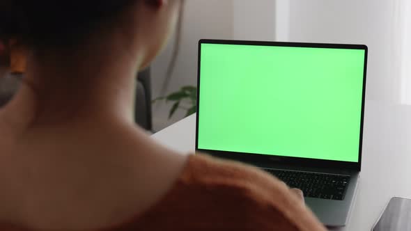 Young Asian woman using laptop computer at home with green blank monitor screen.