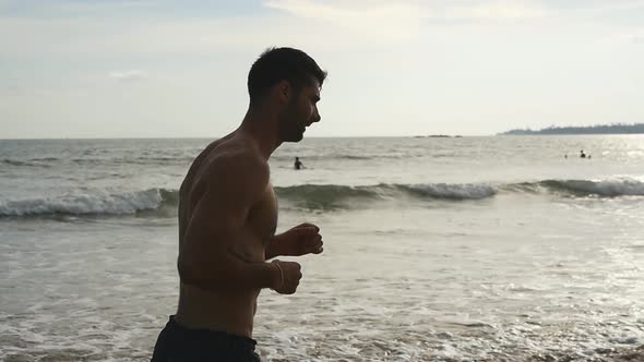 Young Sporty Man Runs Along Ocean Shore. Athletic Handsome Guy Jogs at Beautiful Seascape Background