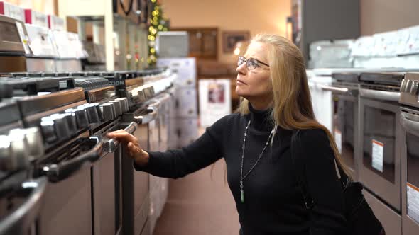 Pretty mature blonde woman looking at the features and benefits of a gas stove in a kitchen applianc
