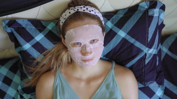 A Young Woman Laying on a Bed with a Cosmetical Face Mask on Her Face. Skincare Concept