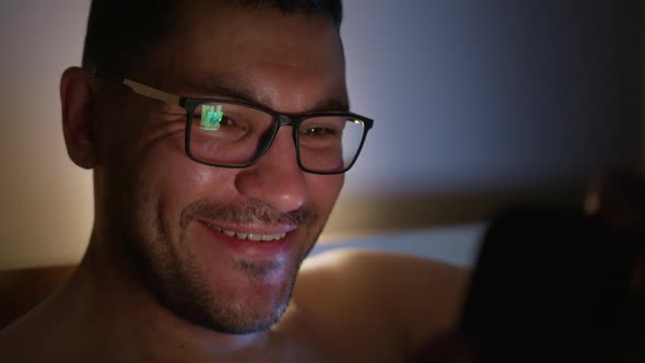 Young Man in Bed Looks at the Screen of His Smartphone