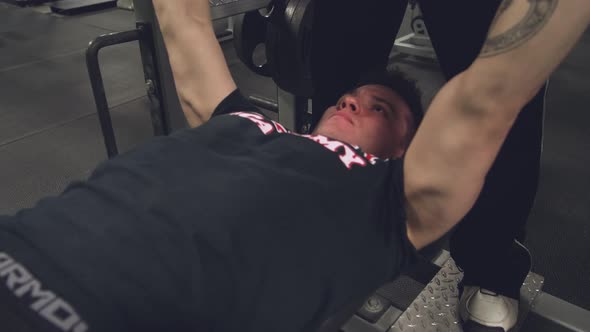 Wide angle shot of a young MMA fighter struggling to complete a bench press set during a workout ses